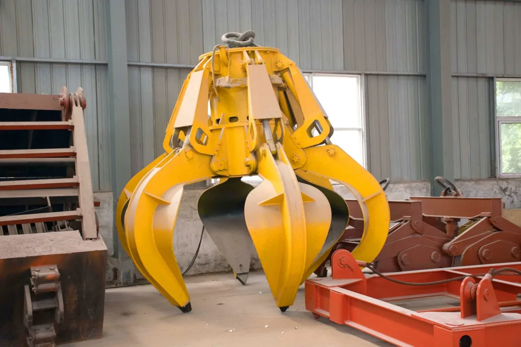 Yellow multi-tine grab with hydraulic cylinders in a workshop