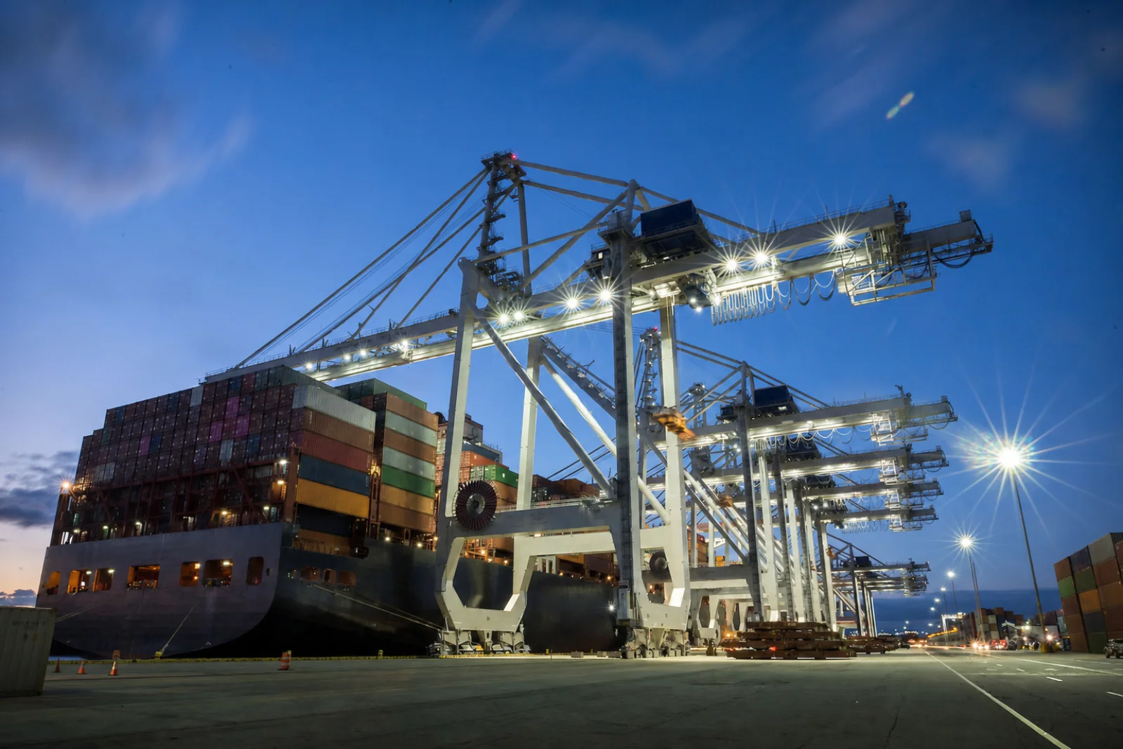 Ship-to-shore container cranes standing along a berthed container ship at night