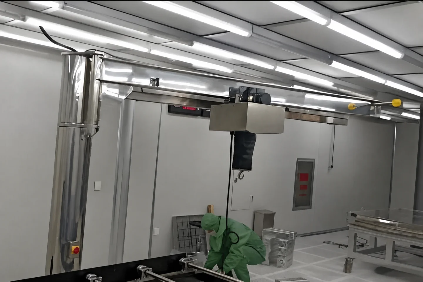 Cleanroom worker servicing equipment beneath a stainless jib crane and enclosed hoist
