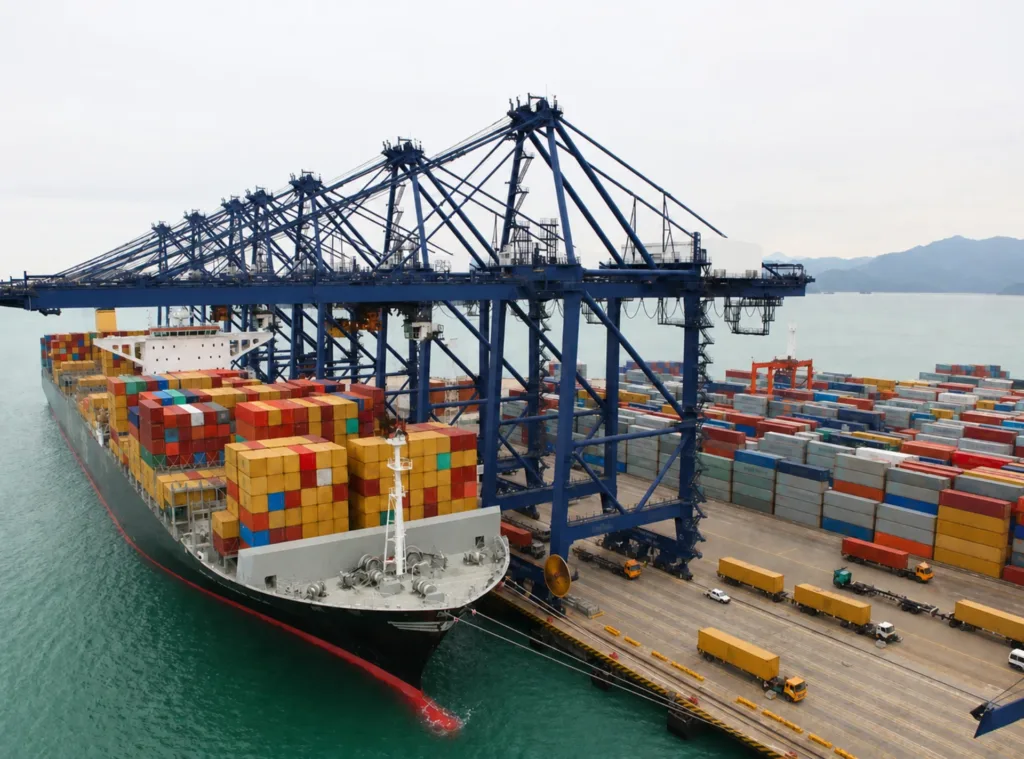 Blue ship-to-shore cranes spanning a container vessel and terminal vehicle lanes beside the quay