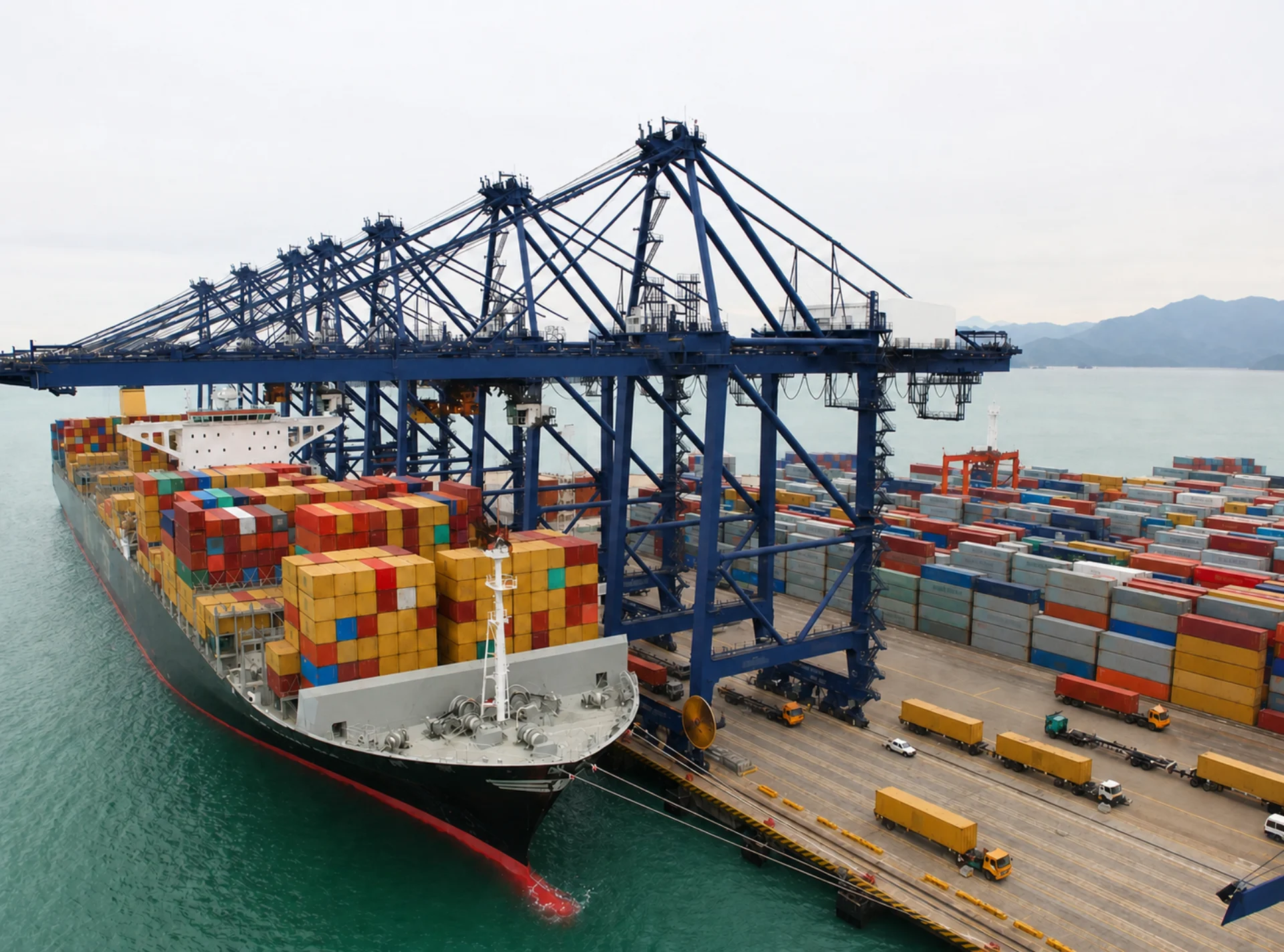 Container vessel alongside ship-to-shore cranes, yard stacks and terminal vehicles
