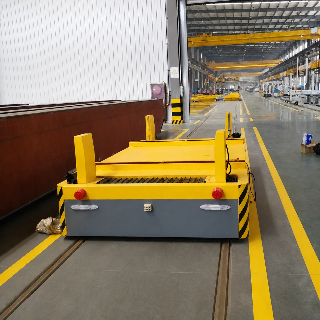 Rail-guided transfer vehicle beside production equipment in a factory