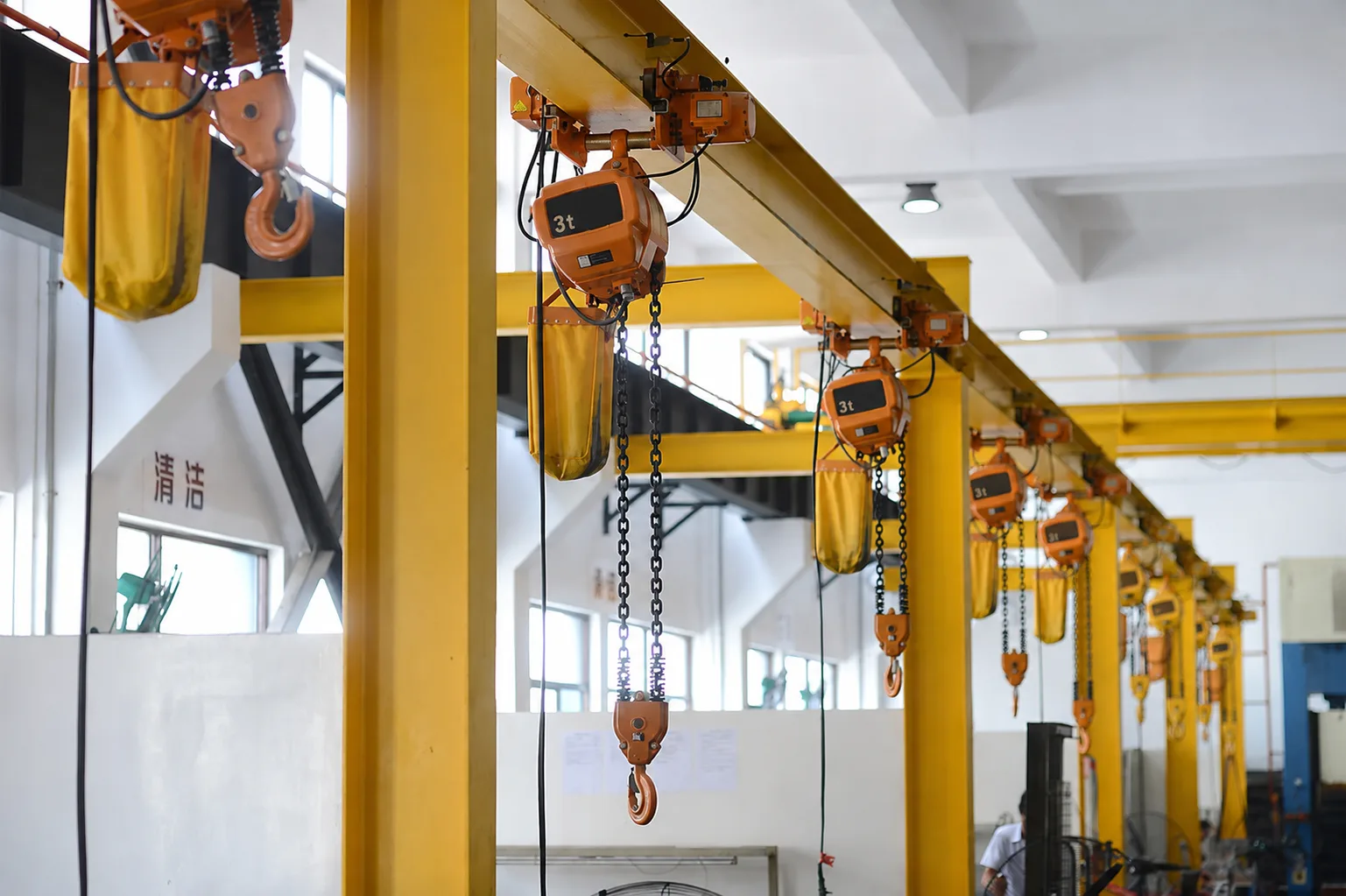 Installed row of electric chain hoists with trolleys, load chains, chain bags and hooks on a workshop monorail