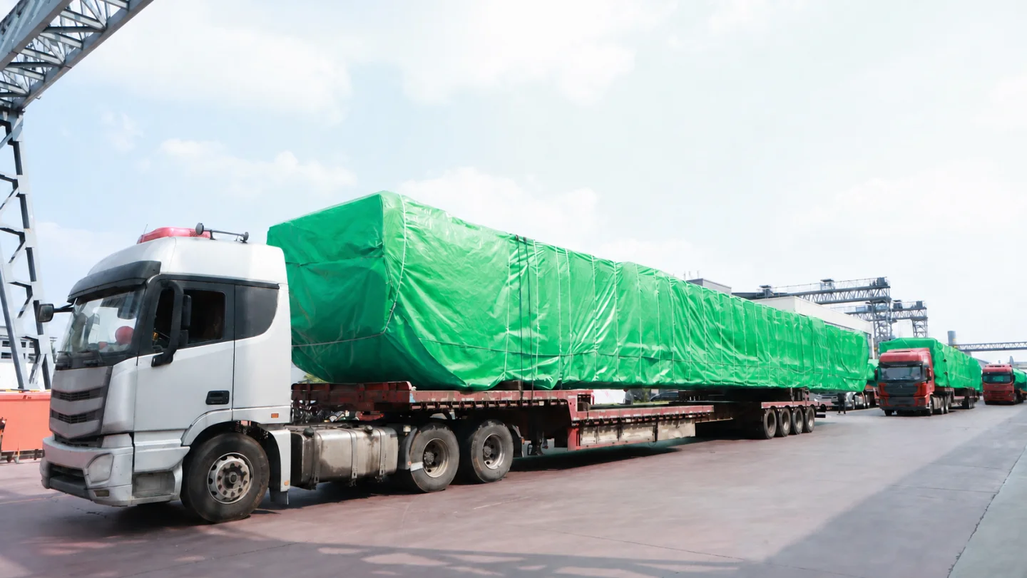 Wrapped crane loads secured on flatbed trucks in an outbound convoy