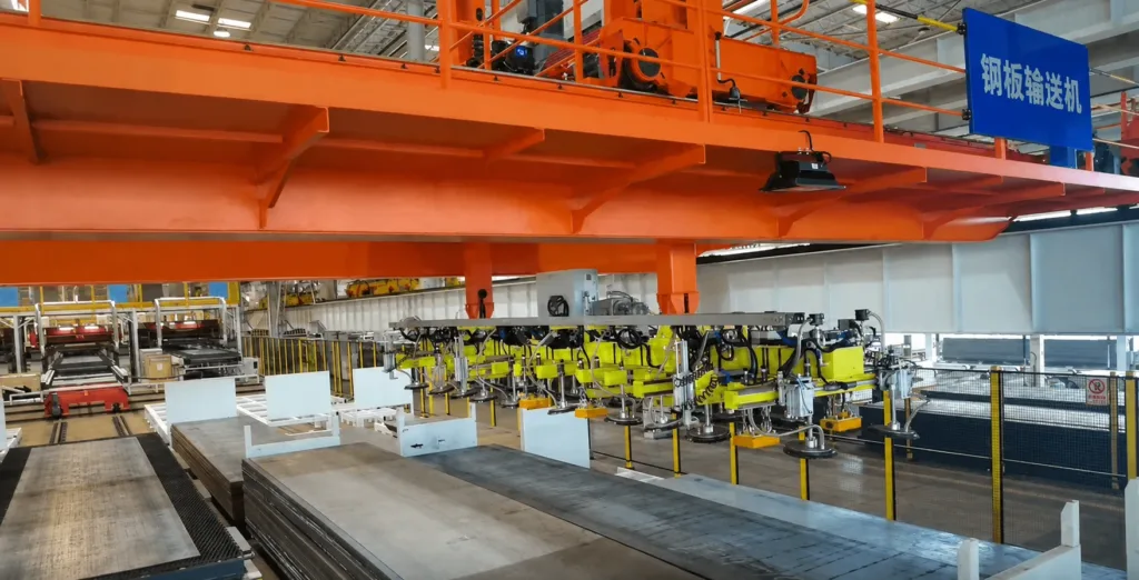 Vacuum lifting attachment above steel plates beneath an orange overhead crane