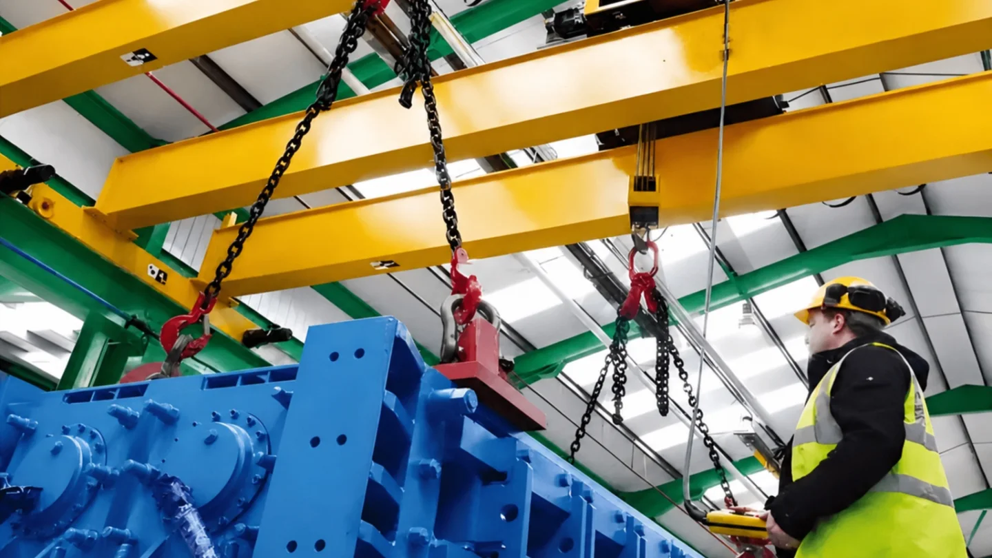 Operator positioning heavy machinery with chains beneath an overhead crane