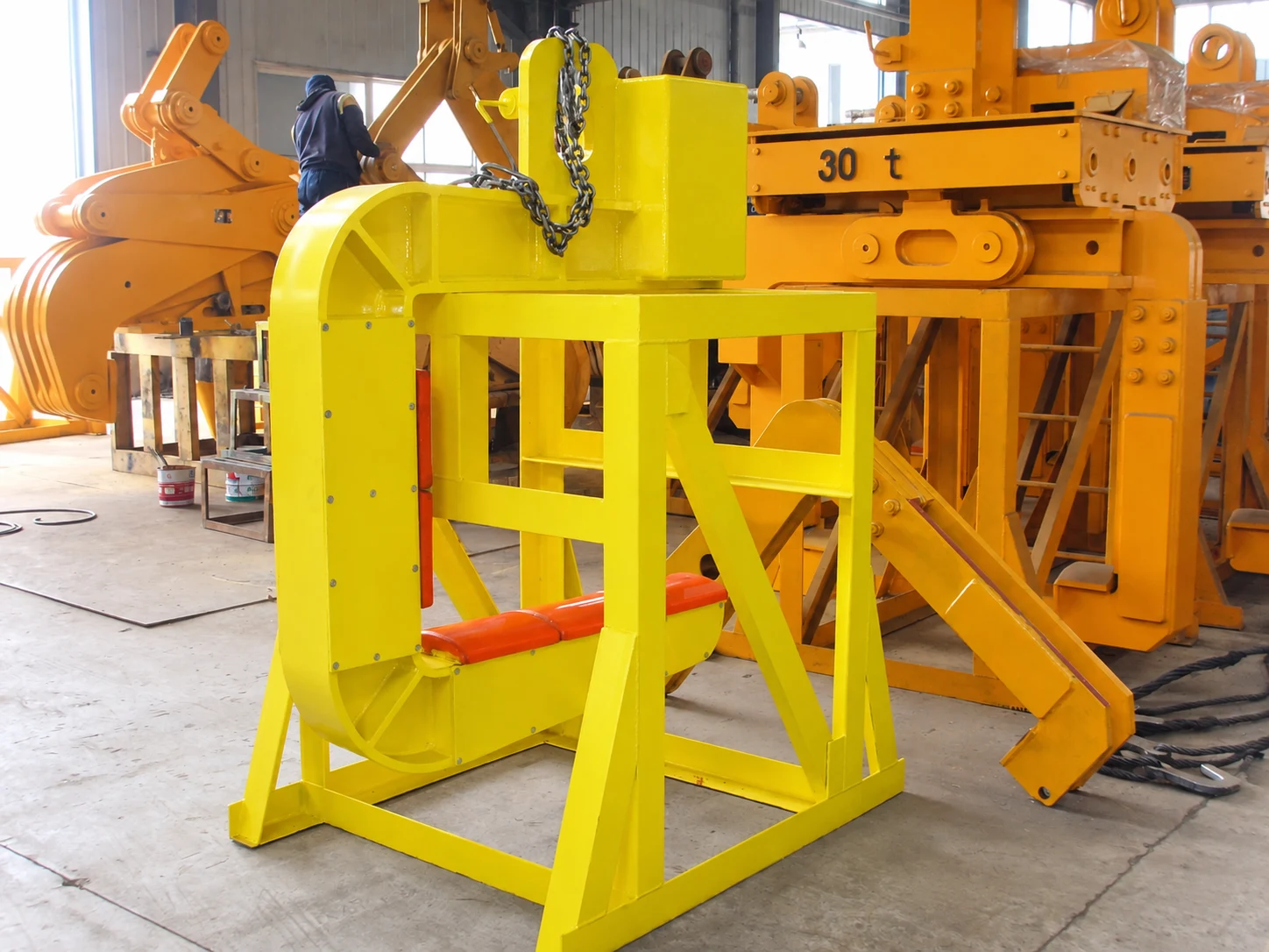 Single-arm C-hook with protective pads and counterweight resting on a storage stand in a workshop