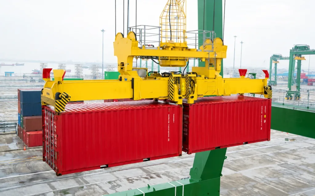 Twin-lift spreader lifting two red 20 foot containers end-to-end