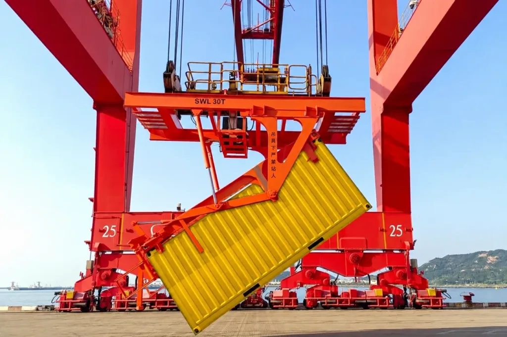 Dedicated tipping attachment tilting a yellow container below a gantry crane