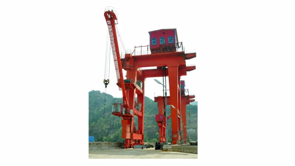 Outdoor dam gantry crane with tall portal legs, an auxiliary boom and rail-mounted travelling assemblies
