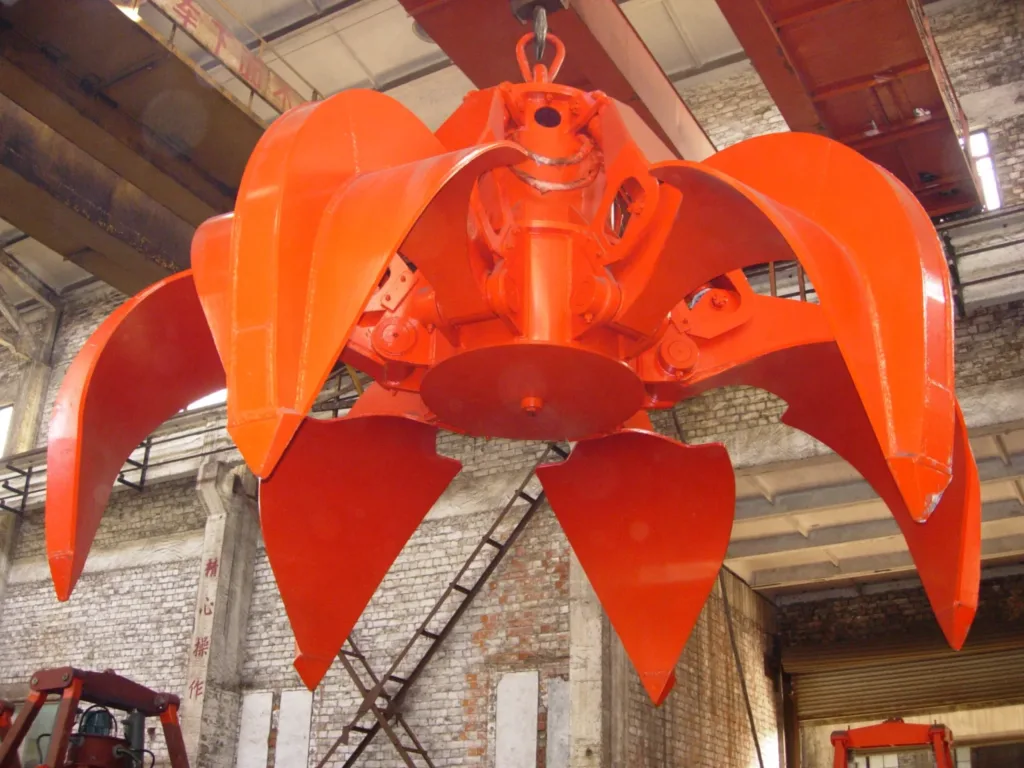 Orange multi-tine grab suspended with its jaws open in a workshop