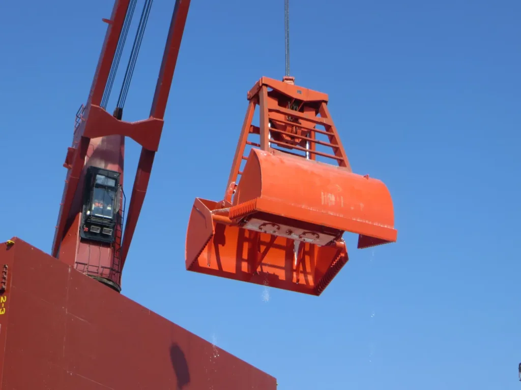 Orange radio-controlled clamshell grab suspended from a ship crane