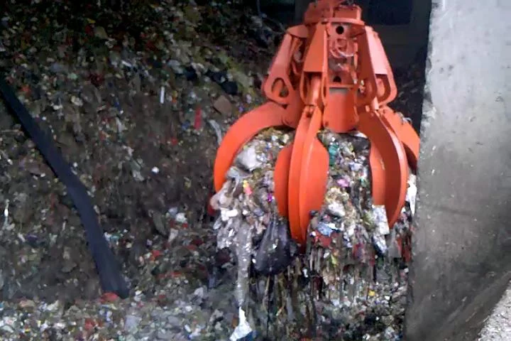 Red multi-tine grab carrying mixed waste in a bunker