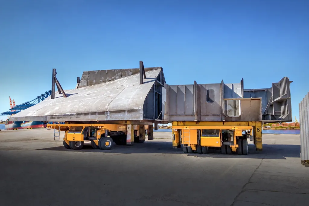 Two coupled hydraulic platform transporters carrying a wide ship section