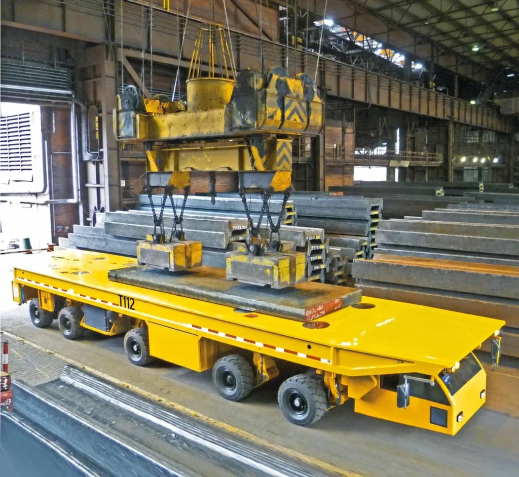 Multi-axle platform transporter receiving a steel slab from overhead lifting equipment