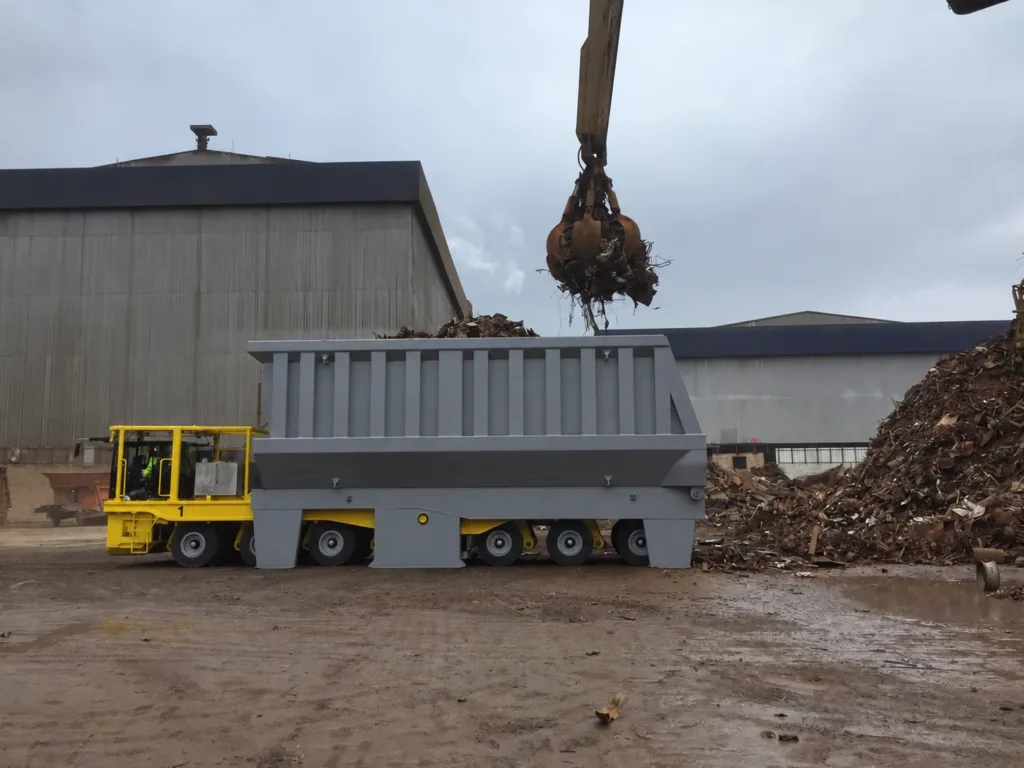 Purpose-built wheeled scrap carrier with a high-sided container being loaded by a grab
