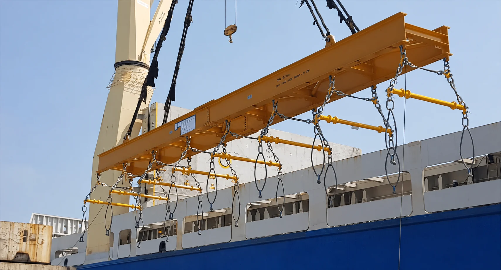 Main lifting beam suspended above a ship with multiple transverse spreader beams and lower rigging, unloaded