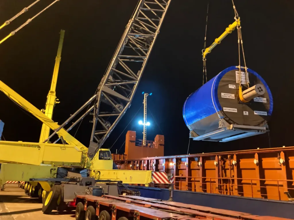 Yellow spreader beam and rigging lifting a wrapped paper dryer at night