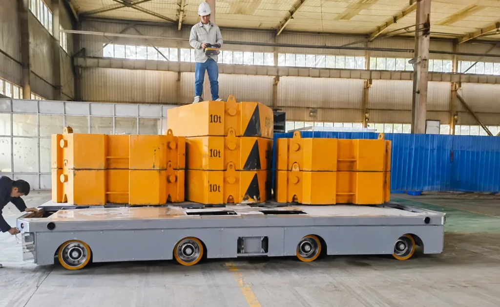 Gray platform with exposed wheel modules beneath orange test weights in a supplier workshop