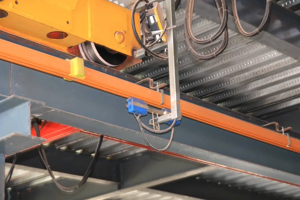 Enclosed conductor rail with blue current collectors and a towing bracket below a crane end carriage