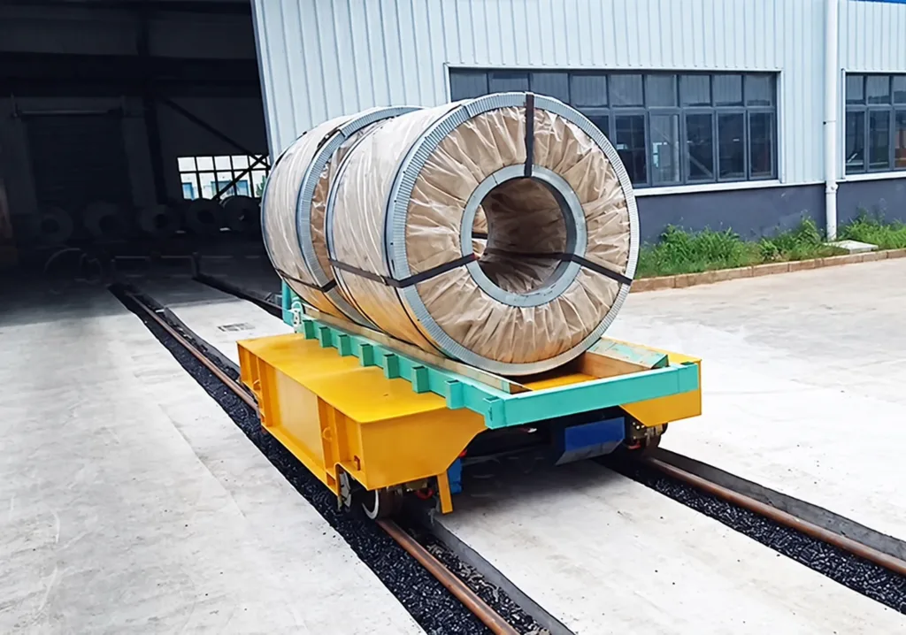 Wrapped steel coil on a green saddle mounted on a yellow rail transfer cart