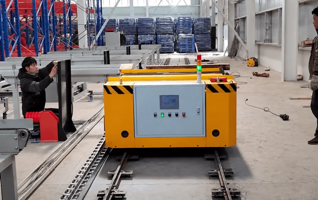 Yellow rail-guided vehicle with local display and buttons beside fixed conveyor stations