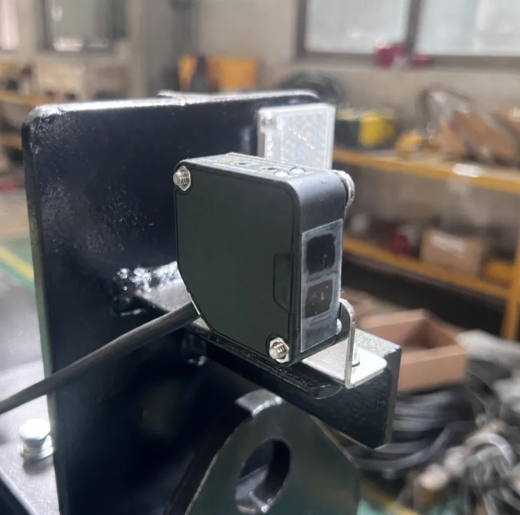 Photoelectric sensor on a steel mounting bracket beside a reflector