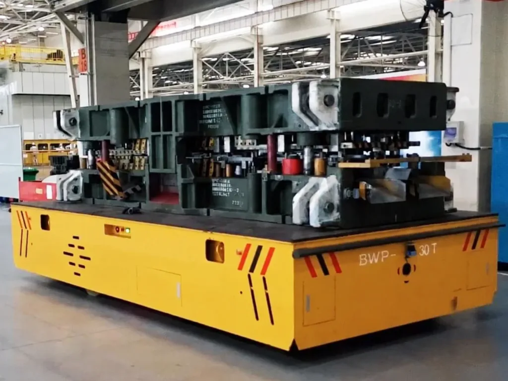 Large industrial die supported on a yellow trackless transfer cart in a workshop