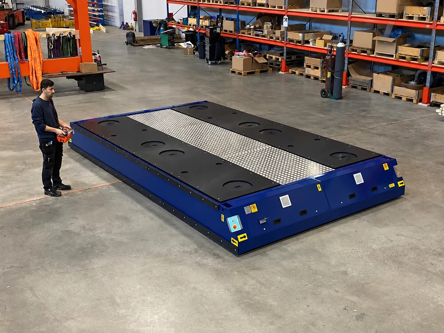 Low-profile blue electric transporter with an operator using a handheld remote in a workshop