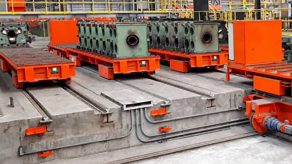 Orange rail-guided transport vehicles and roller-deck handoff stations inside a factory