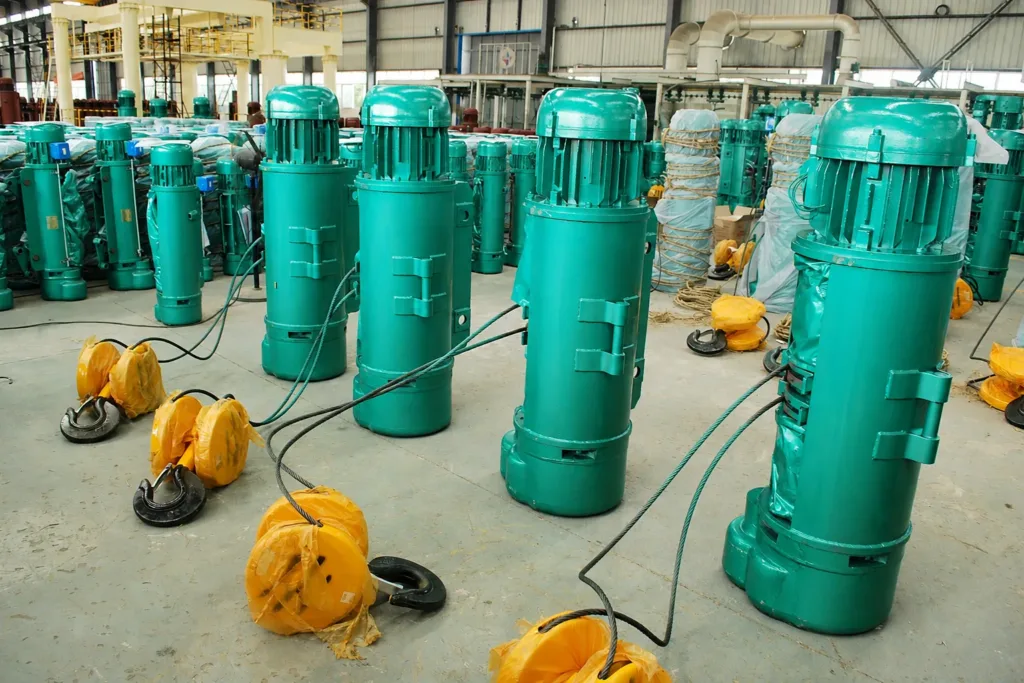 Completed standard electric wire-rope hoists and hook blocks inside a manufacturing workshop